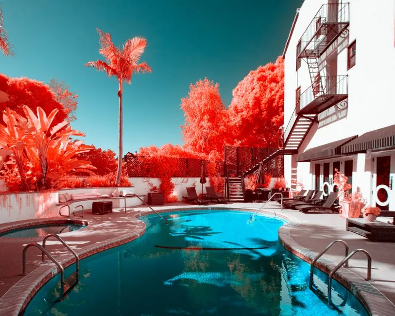 A striking infrared image of an urban poolside scene featuring vibrant red foliage and a blue pool.